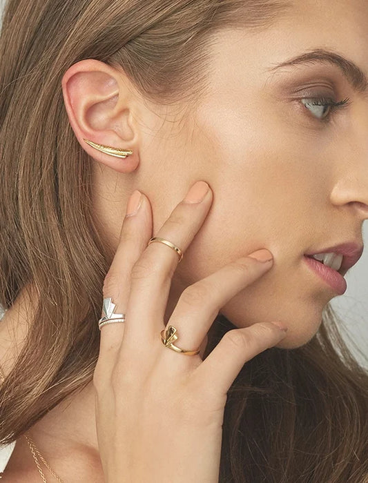 A close-up of a woman's ear and hand showcasing gold jewellery, including a curved gold fan ear pin, and a gold and silver fan ring