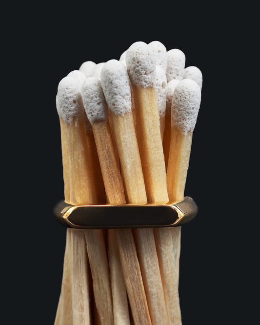 A small bunch of white tipped matches held together with a gold slim signet ring around their middle on. black background