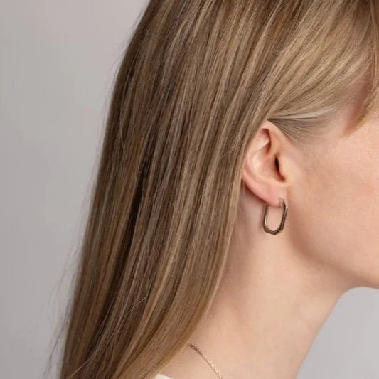 A close-up side profile of a woman with long blonde hair wearing a square hoop earring.