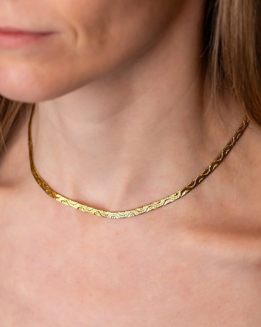 A close-up of a woman wearing a delicate textured gold chain necklace.
