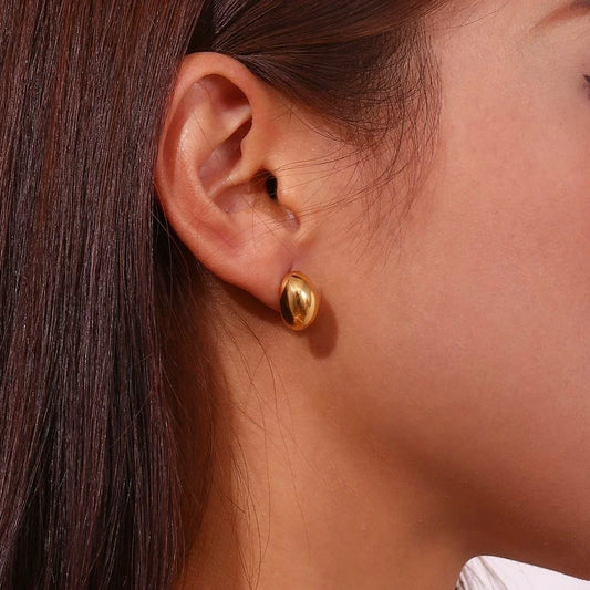 Close-up of a person with dark hair wearing a gold bubble stud earring.