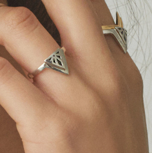 A close-up of a hand wearing two silver Rise rings with geometric triangular cutout designs, one on each finger.