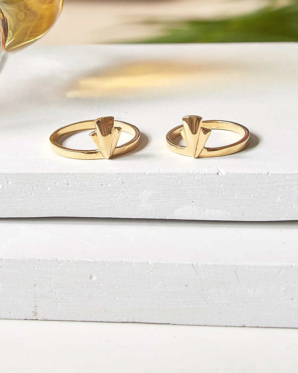 A pair of gold-toned fan ring earrings with a triangular fan design, displayed on a white textured wooden block.