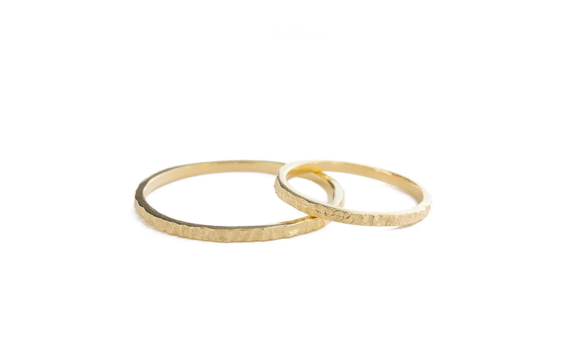 Two thin textured gold rings overlapping on a plain white background.