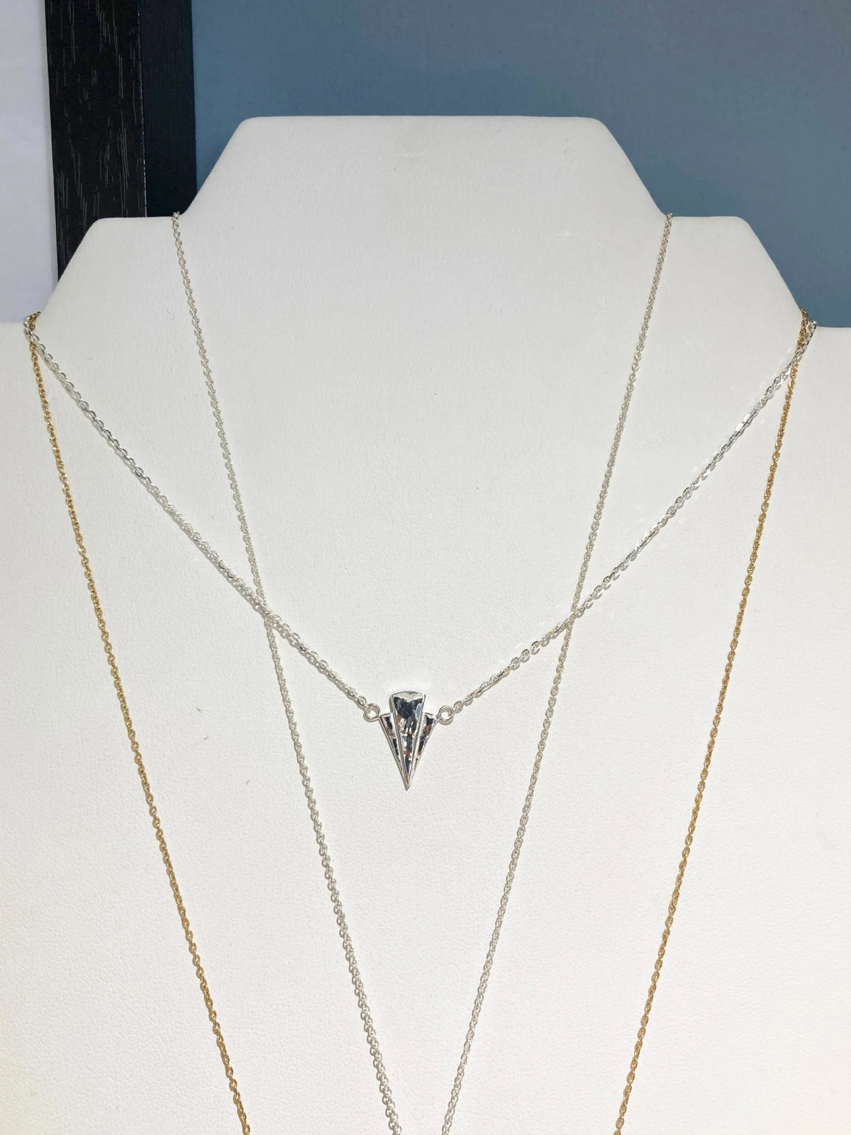 Fan necklace displayed on a white jewellery display, featuring a silver chain with a fan pendant and two gold-toned chain necklaces layered underneath 