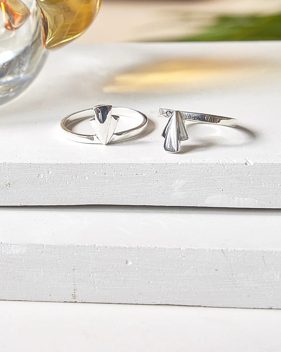 Two silver fan rings with a geometric, fan  design resting on a white wooden surface.