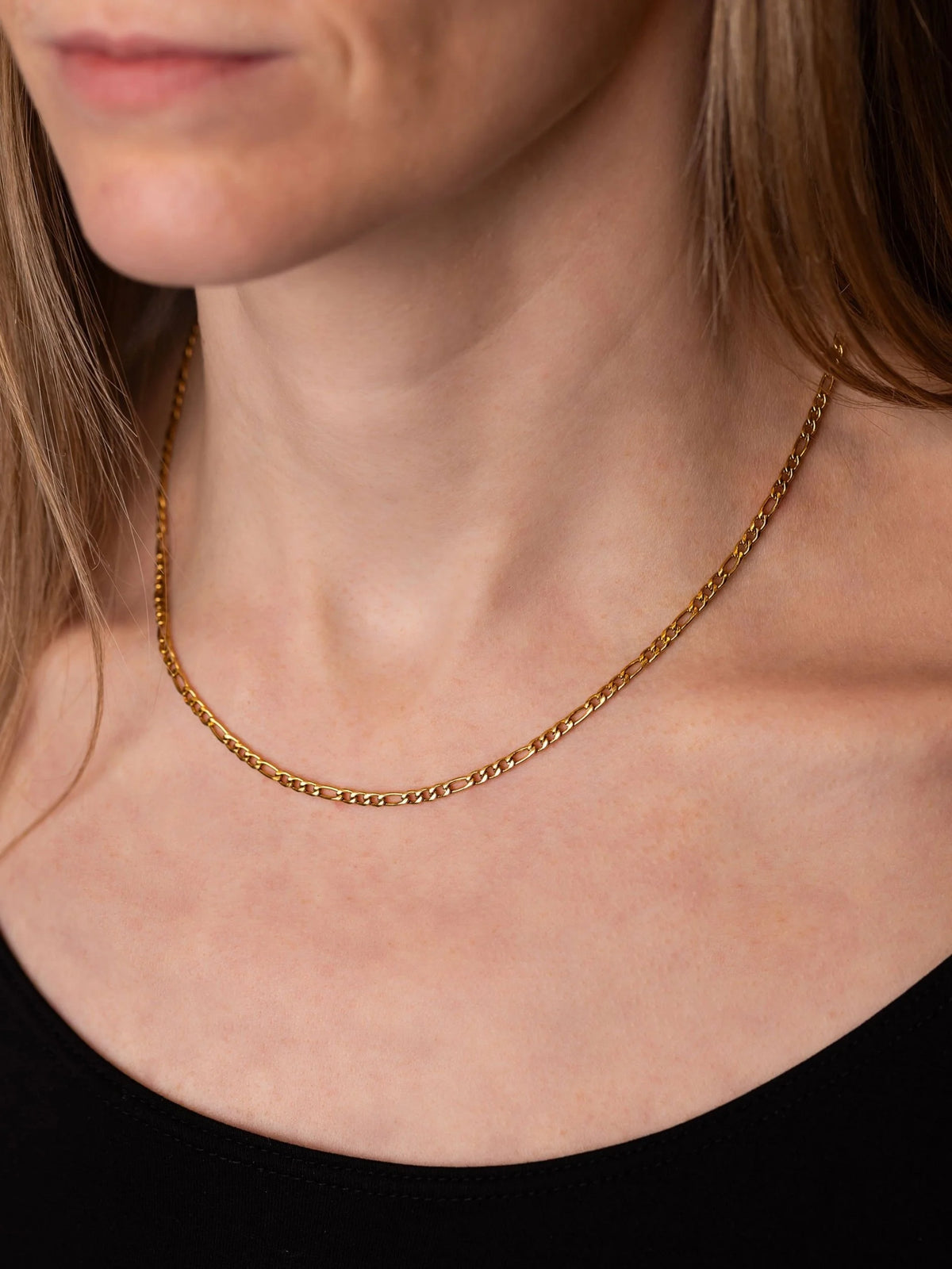 A close-up of a woman's neck and upper chest wearing a Figaro gold chain necklace.