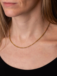 A close-up of a woman's neck and upper chest wearing a Figaro gold chain necklace.