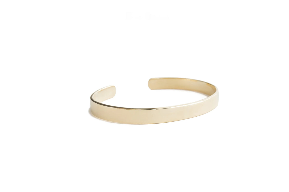 A minimalist, polished gold Foundation plane bangle on a clean white background.