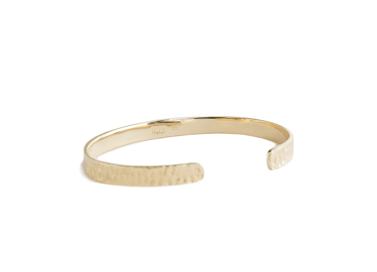 A gold open cuff bangle bracelet with a textured hammered finish on one side and a smooth polished finish on the inside, shown on a plain white background.