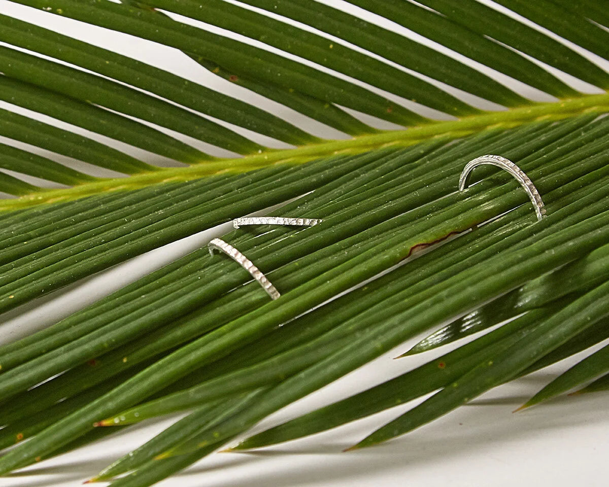 Three silver foundation textured rings displayed on a green palm leaf against a white background.
