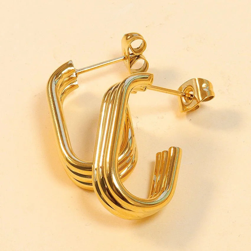 A pair of gold Trio hoop earrings with a layered design and post-back closures, displayed on a light beige background.