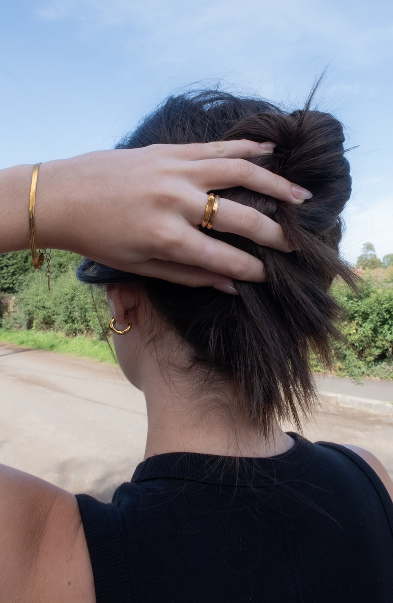 Picture of the back of the head of a model holding a bun up with gold rings and the herringbone bracelet on her wrist