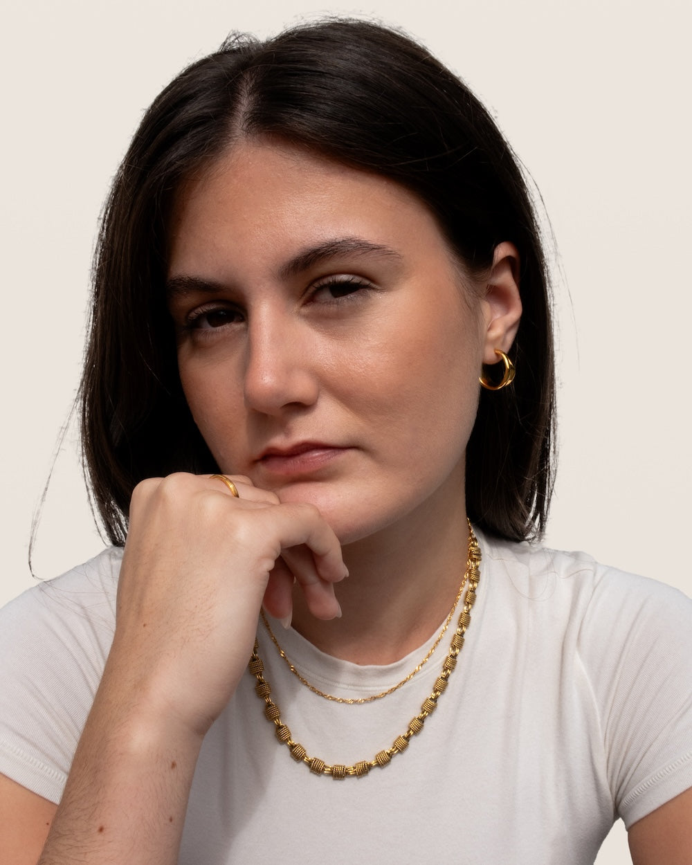 Model wearing a white t shirt with a gold twist chain and chunky woven necklace. Also wearing molten hoops