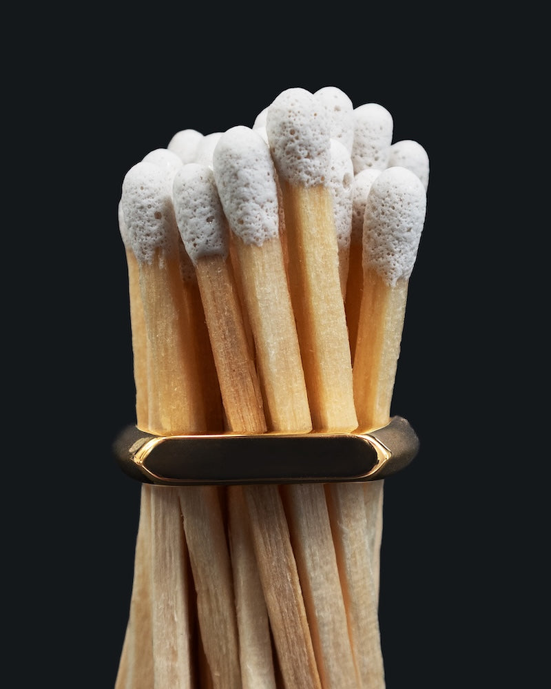 A small bunch of white tipped matches held together with a gold slim signet ring around their middle on. black background 