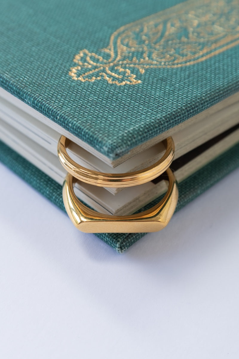 Two gold rings places between the corner pages of a green book.