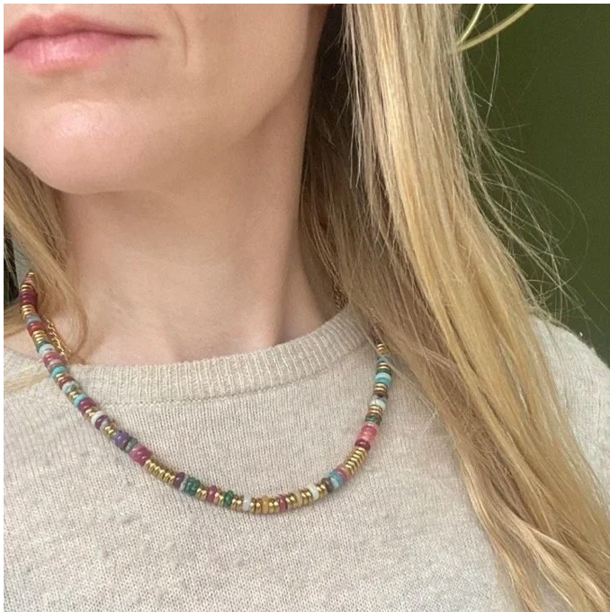 A close-up of a woman wearing a beaded necklace with small multicolored round beads, paired with a light beige knit sweater.