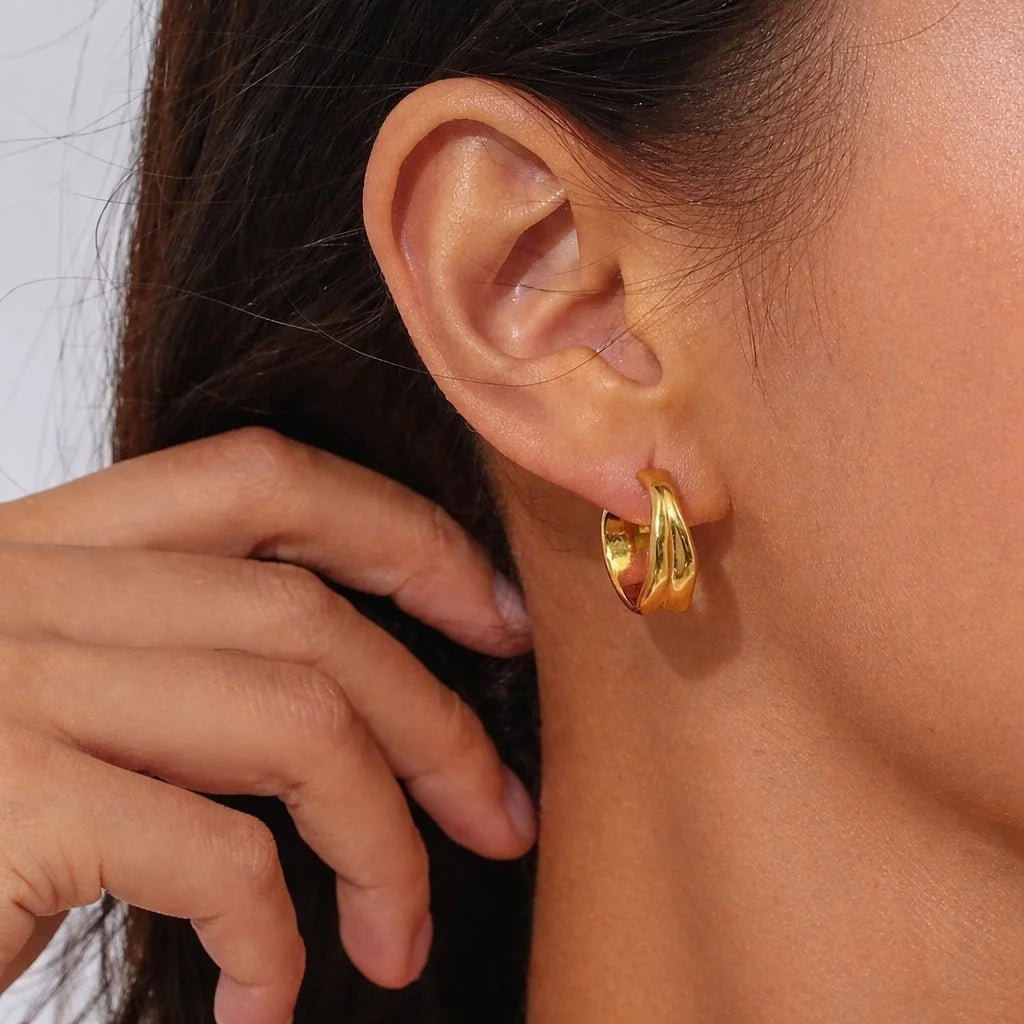 A close-up of a woman's ear wearing a small gold Molten hoop earring, with a hand touching the earring.