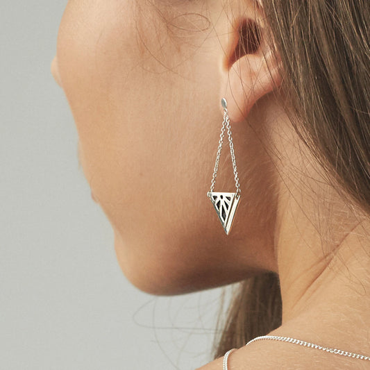 A close-up side profile of a woman wearing a delicate silver Rise earring with a geometric triangular cutout design. Art deco sunrise design