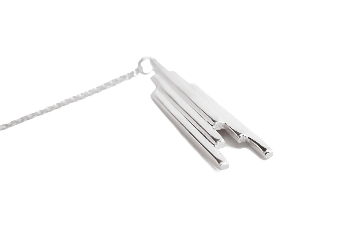 A silver pendant necklace featuring three gradated polished bars of varying lengths, suspended from a delicate silver chain against a solid white background. Art deco style design