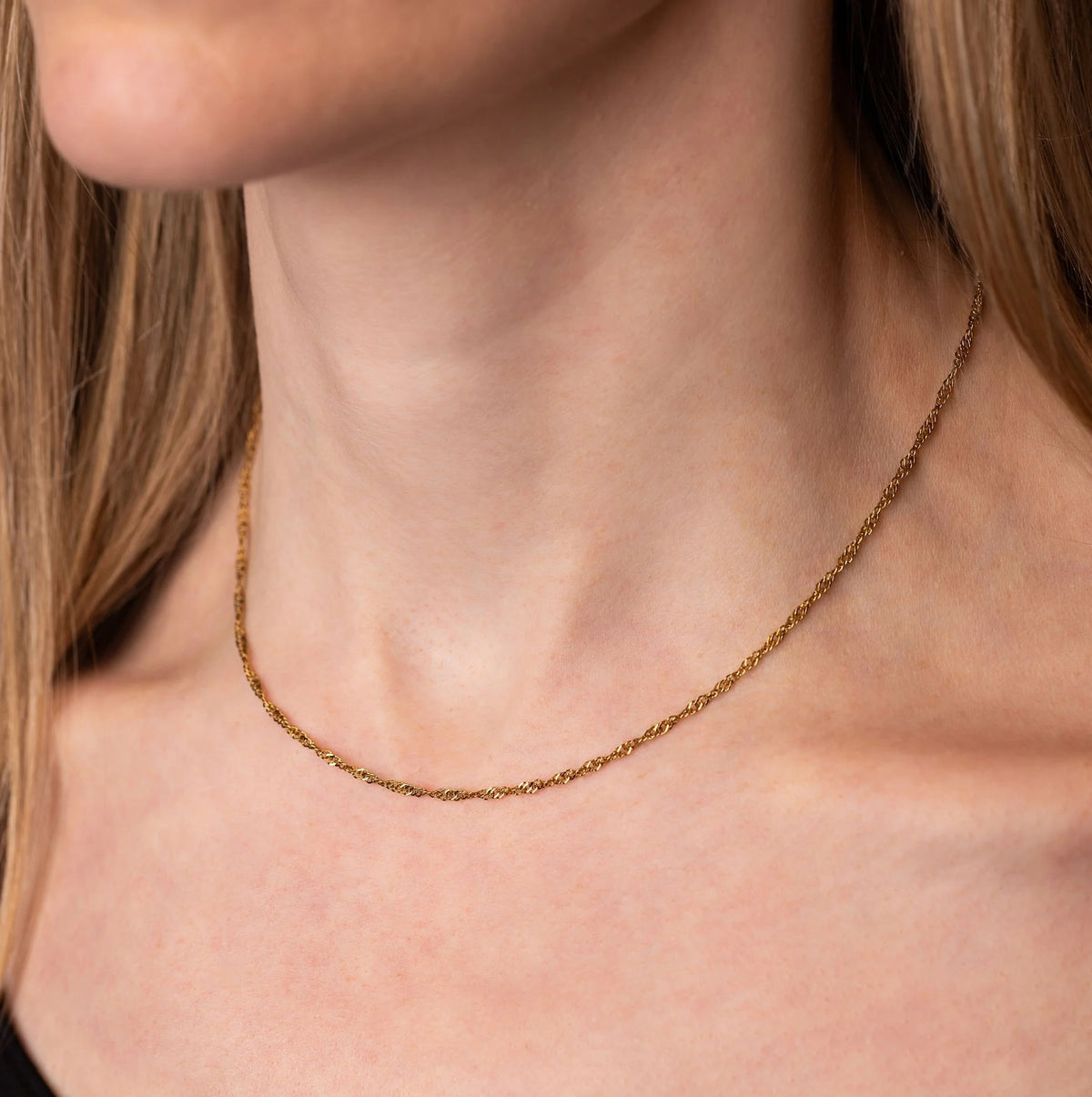 A close-up of a model's neck and collarbone wearing a delicate, thin gold Twist chain necklace.