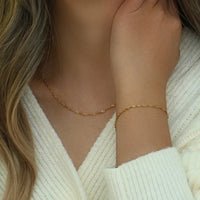Close-up of a person wearing a gold Twist necklace and bracelet against a neutral background