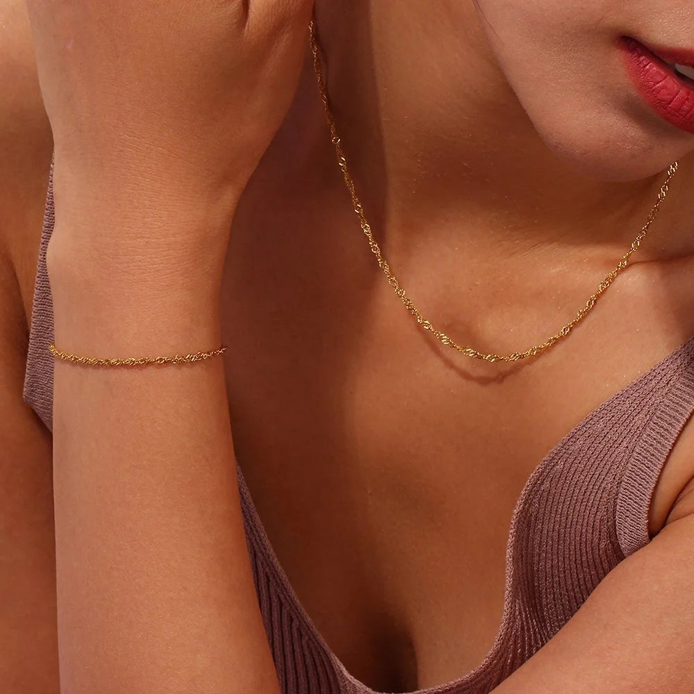 Close-up of a woman wearing a Twist gold necklace and bracelet on a warm-toned background