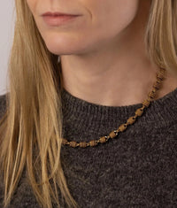 A close-up of a woman wearing a textured Woven Chunky gold chain necklace with cylindrical links, paired with a dark grey knit sweater.