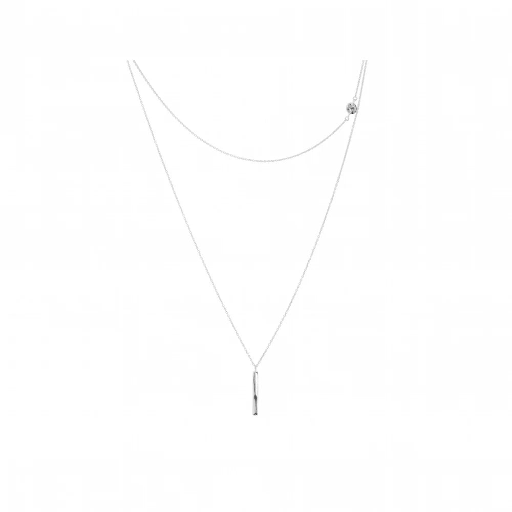 A delicate silver necklace featuring a long chain with a slim vertical bar pendant at the bottom and a small round disk detail on the upper right side, shown against a plain white background.
