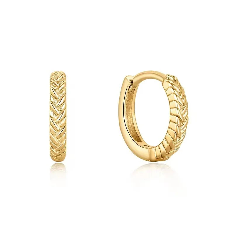 A pair of gold Braid huggie hoop earrings with a textured chevron pattern, shown from both front and side angles on a white background with soft reflections.