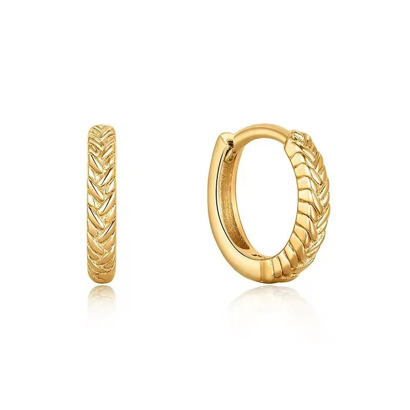 A pair of gold huggie braid hoop earrings with a textured chevron pattern, shown from both front and side angles on a white background with a soft reflection.