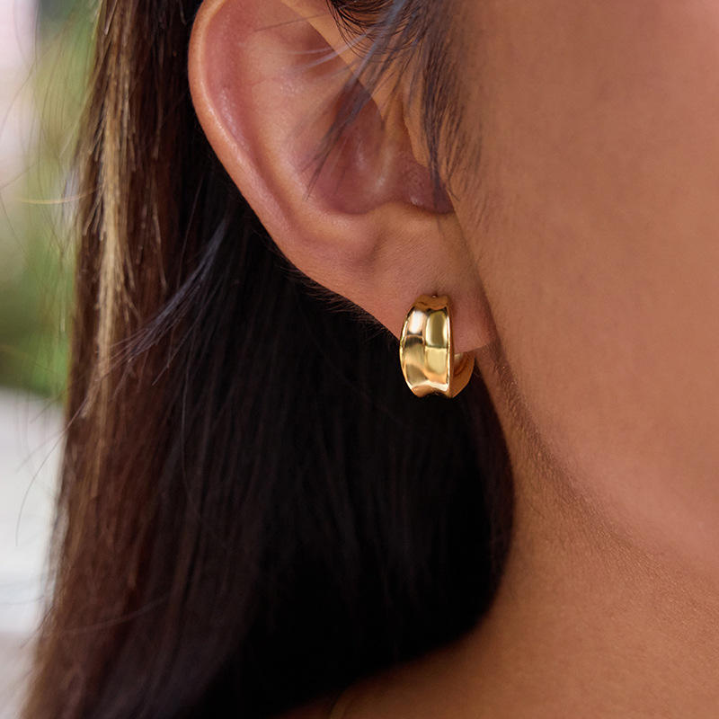 Gold sculpted hoop earring worn by a person with dark hair.