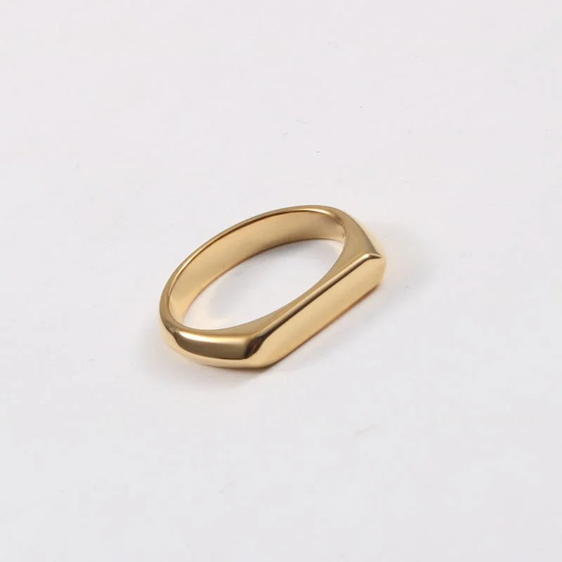 A gold slim signet-style ring with a polished, rounded rectangular face, shown on a clean white background.